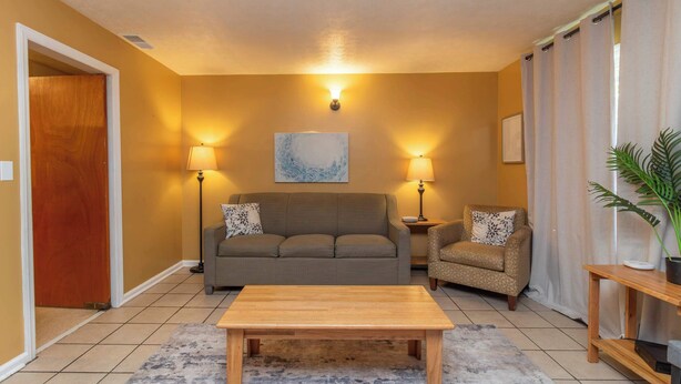 Een woonkamer met een bank, twee fauteuils, een salontafel, een lamp, een schilderij en een plant in pot.