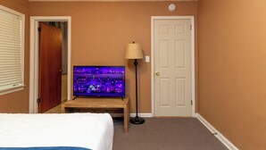 Een hotelkamer met een bed, een televisie op een standaard, een deur en een lamp.