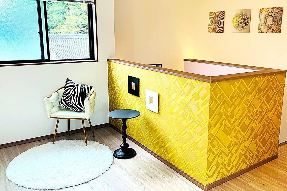 Een kamer met een geel tussenschot, een witte stoel met een kussen met een zebraprint, een ronde tafel en een raam met uitzicht op groen.