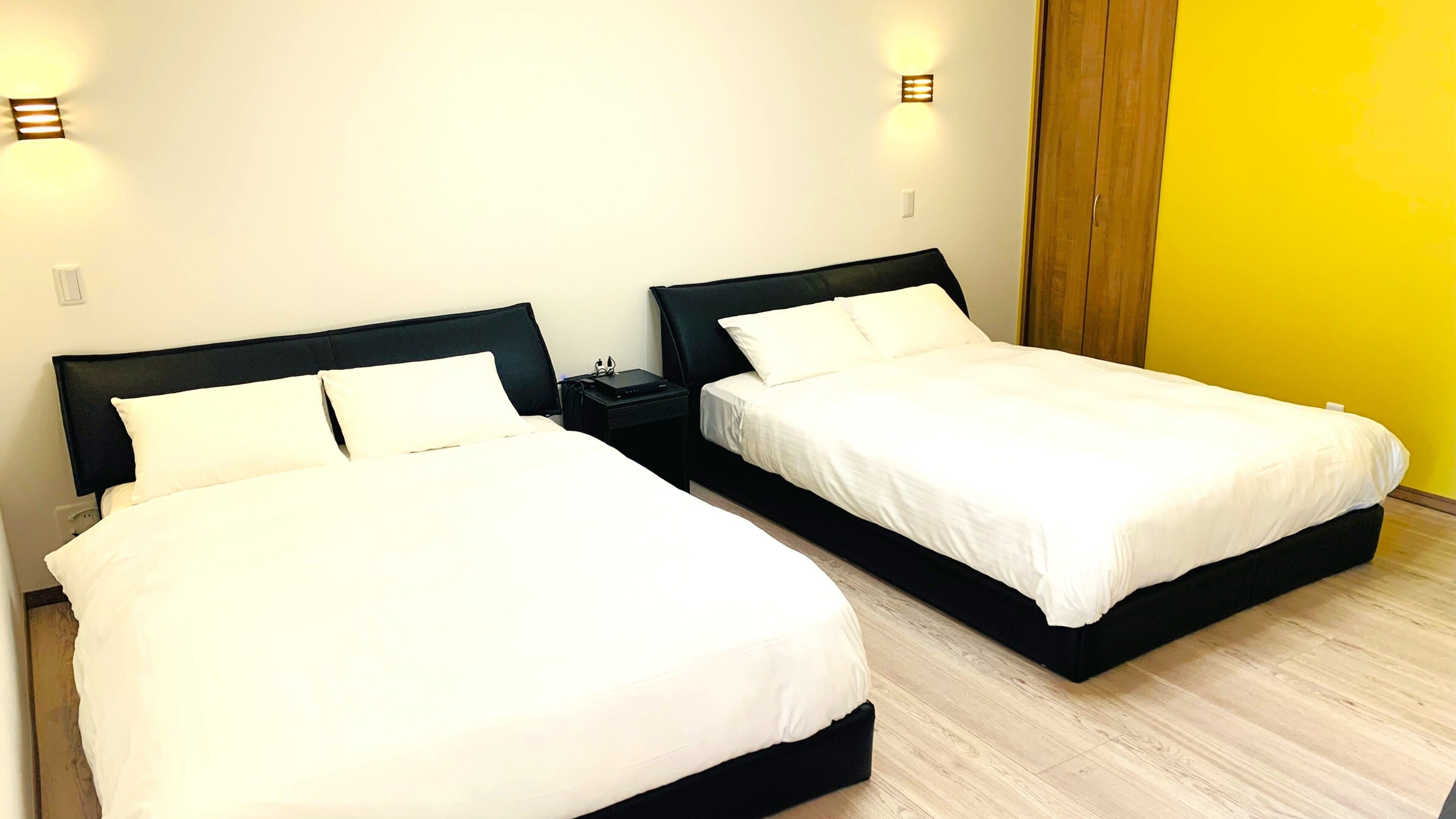 Two twin beds with black headboards, white bedding, bedside tables, and wall-mounted lights.