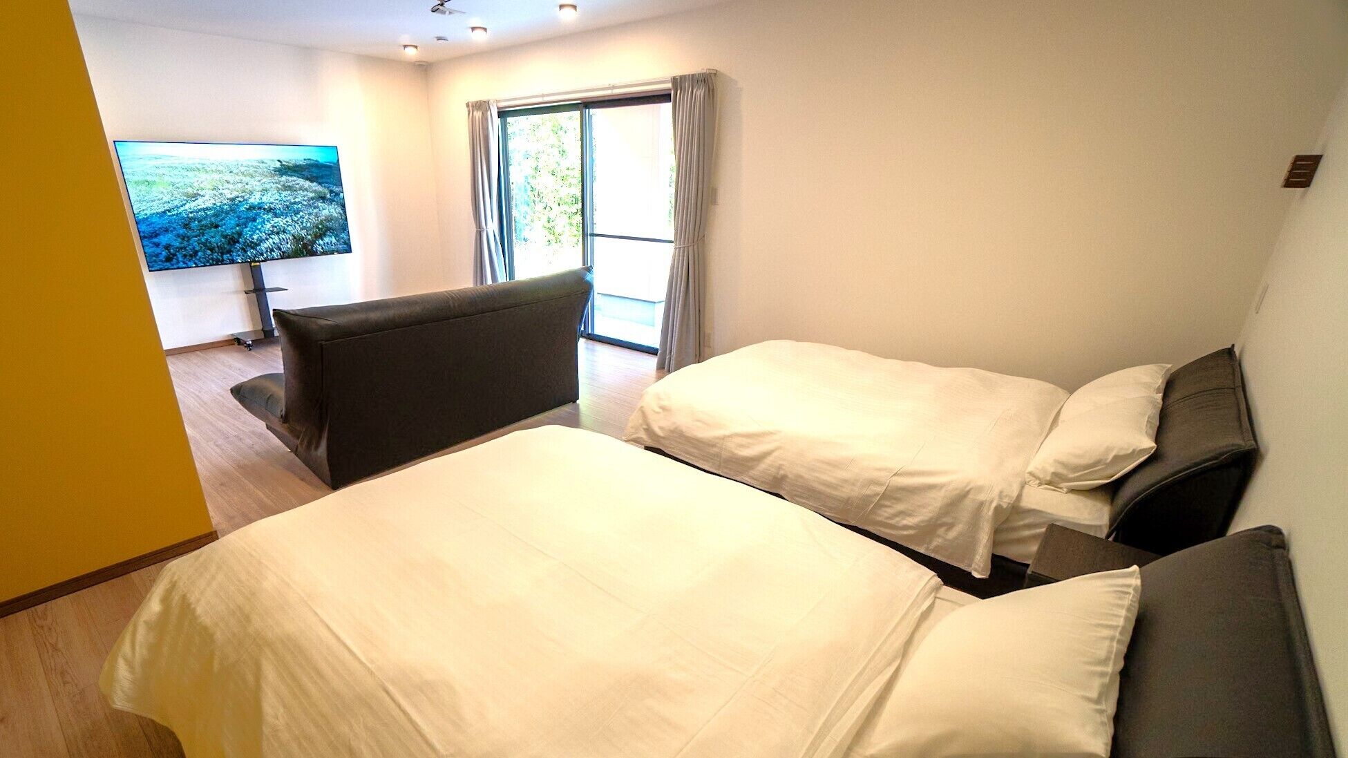 A hotel room with two beds, a sofa, a TV, and a window with curtains.