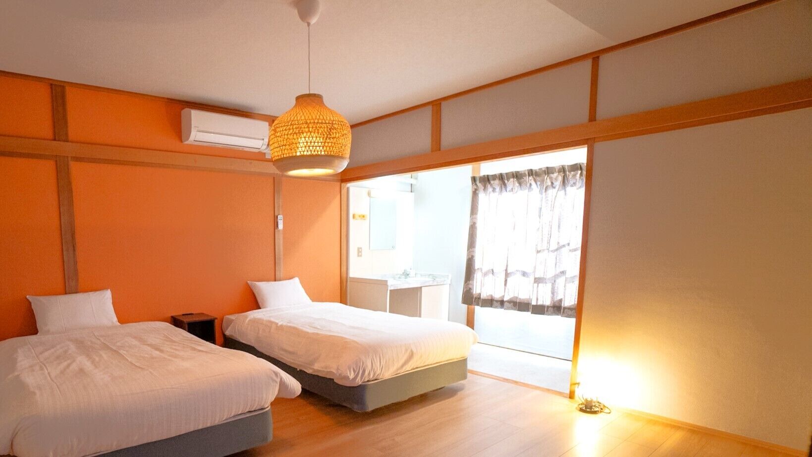 A room with two beds, a hanging light fixture, an air conditioning unit, and a window with curtains.