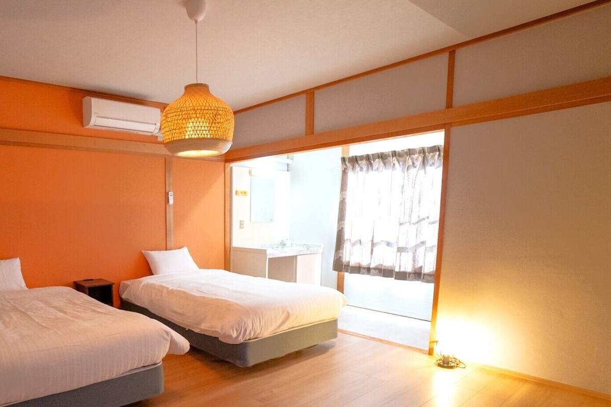 Een kamer met twee bedden, een hanglamp, een airconditioning en een raam met gordijnen.