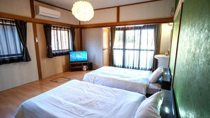 Habitación de hotel con dos camas, televisión, lavamanos y un amplio ventanal con cortinas.