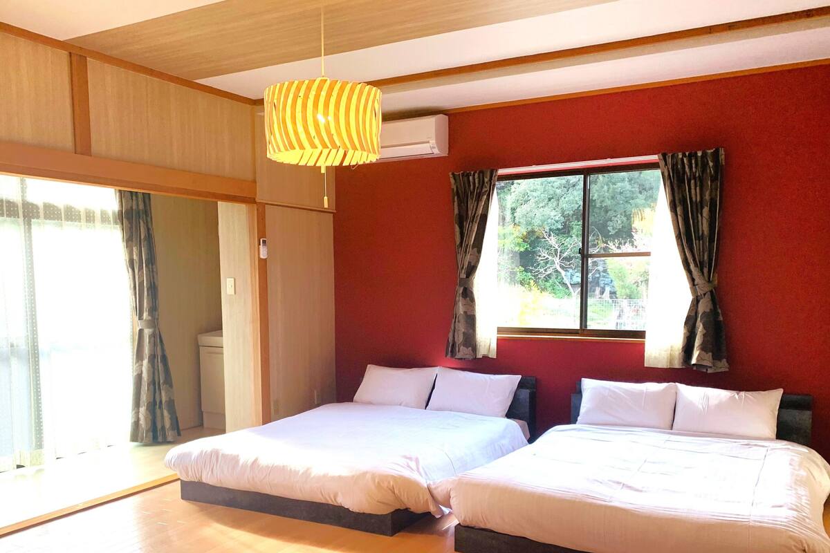 Een slaapkamer met twee bedden, een houten plafond en een groot raam met gordijnen.