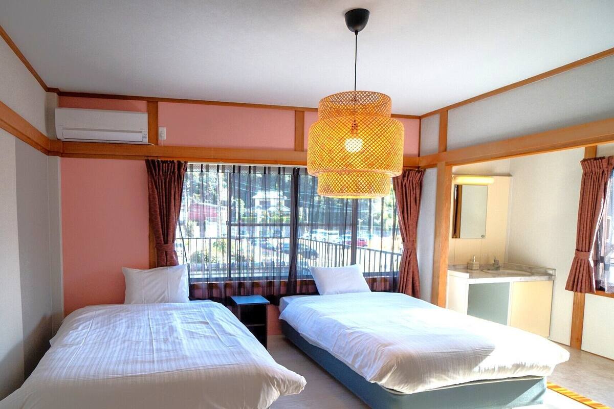 Een hotelkamer met twee bedden, een raam met gordijnen, een hanglamp en een klein nachtkastje.