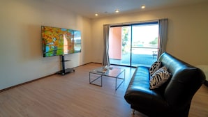 A modern living room with a flat-screen TV, a glass coffee table, a leather sofa, and a sliding glass door leading to an outdoor area. - Alloggio Nanki Shirahama (Shirahama)