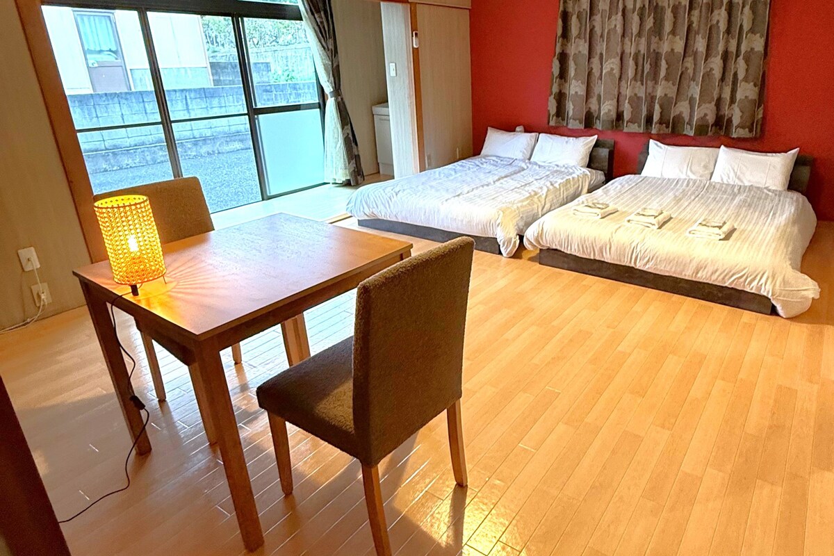 Habitació d'hotel amb dos llits, un escriptori de fusta amb una làmpada, una cadira i vista a l'exterior.
