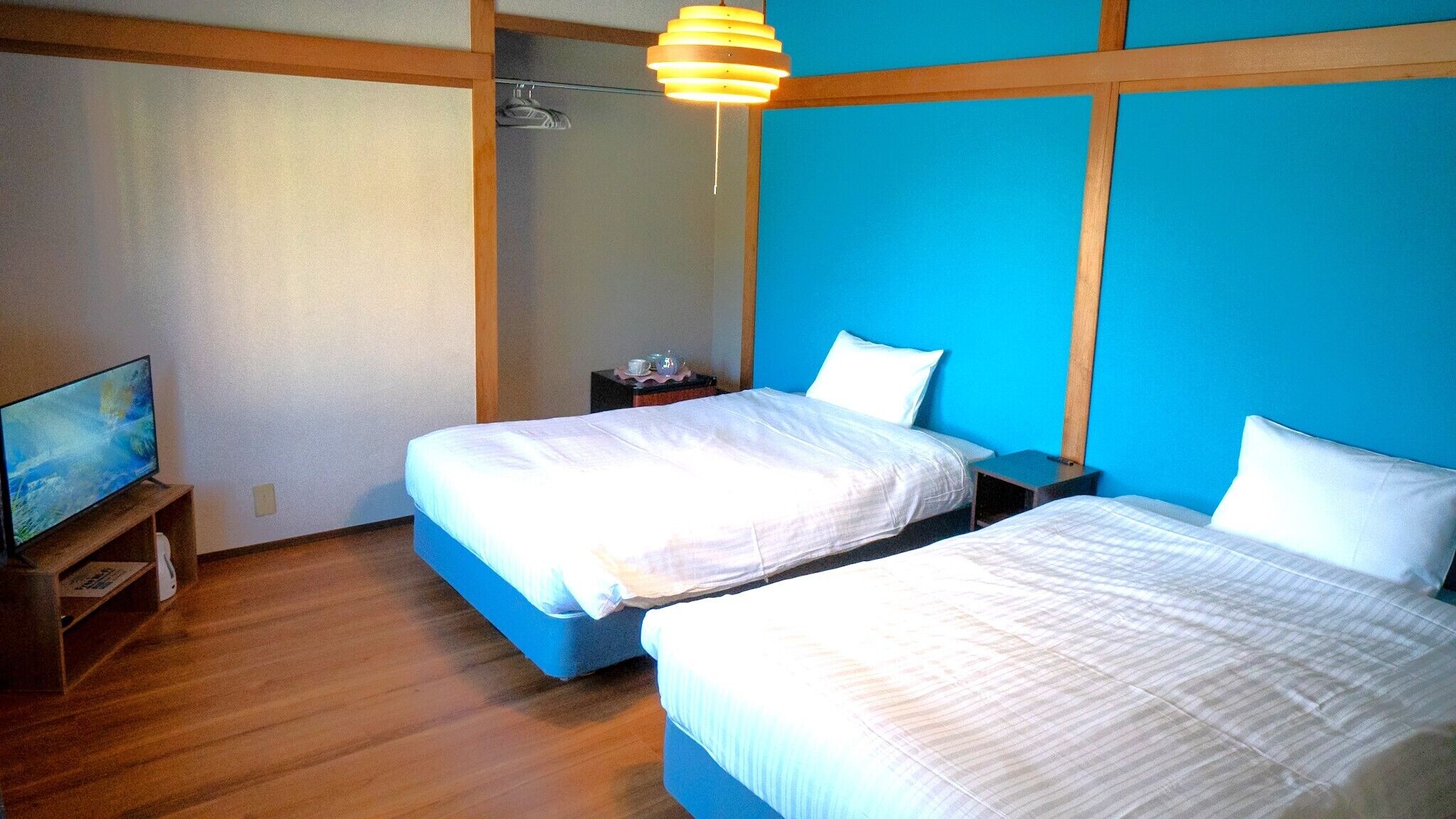 A hotel room with two beds, a television, and a wooden floor.