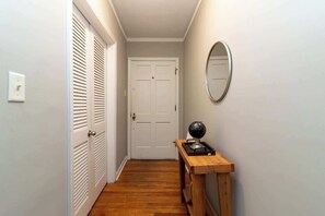 A hallway with a wooden floor, a white door, a wooden side table with a globe, and a round mirror on the wall. - Pet-Friendly Home, Walk to Riverwalk, Free (Columbus)