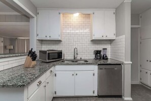 A modern kitchen with white cabinets, a granite countertop, a microwave, a coffee maker, and a dishwasher. - Pet-Friendly Home, Walk to Riverwalk, Free (Columbus)
