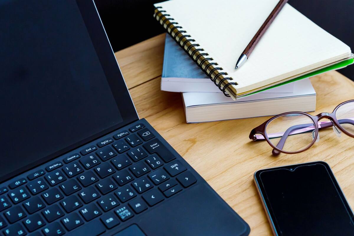Ein Laptop, ein Smartphone, eine Brille und Bücher auf einer Holzoberfläche.