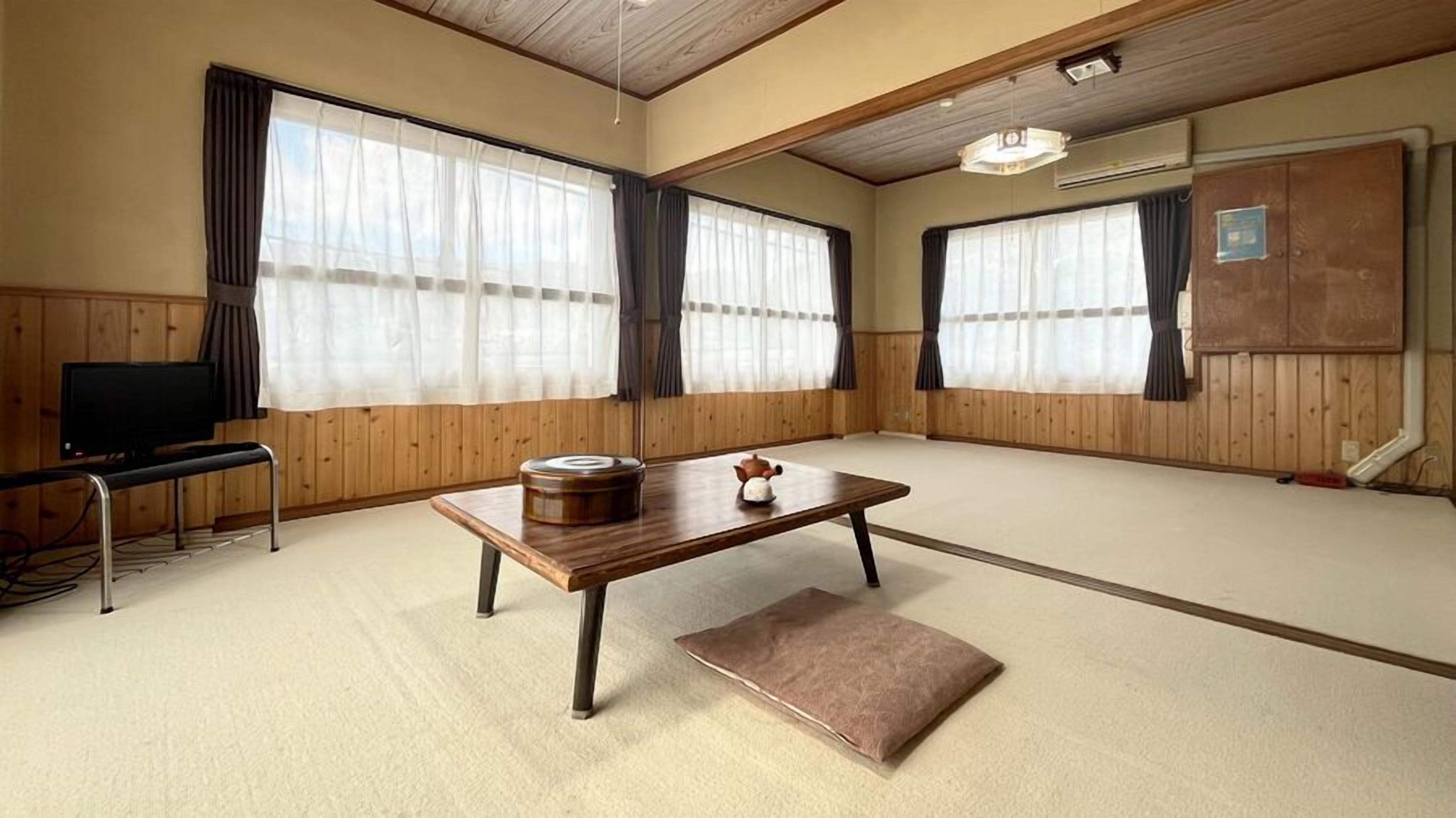 A traditional Japanese-style room with tatami flooring, a low wooden table, a television on a stand, and a cabinet.