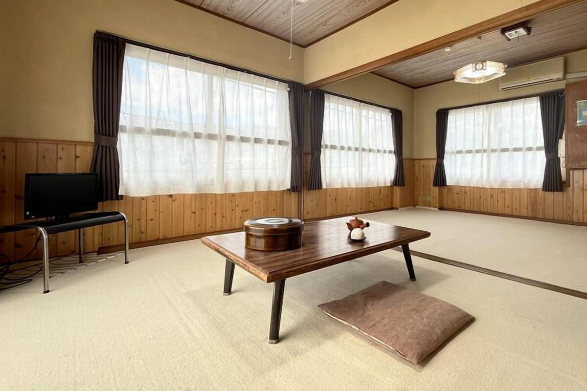 Ein traditioneller japanischer Raum mit Tatami-Bodenbelag, einem niedrigen Holztisch, einem Fernseher auf einem Standfuß und einem Schrank.