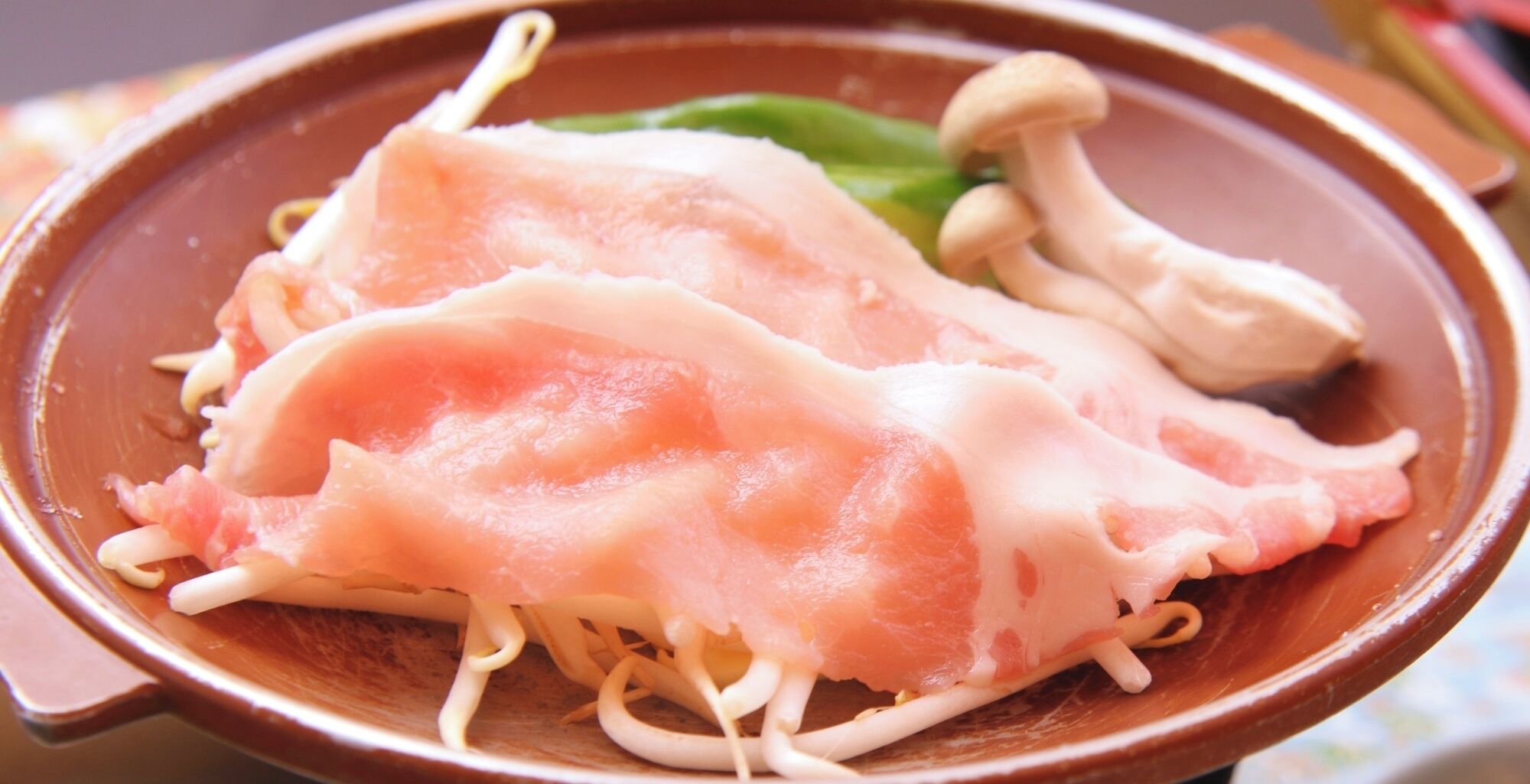 Eine Schüssel mit Scheiben von rosa Fleisch und weißen Pilzen.