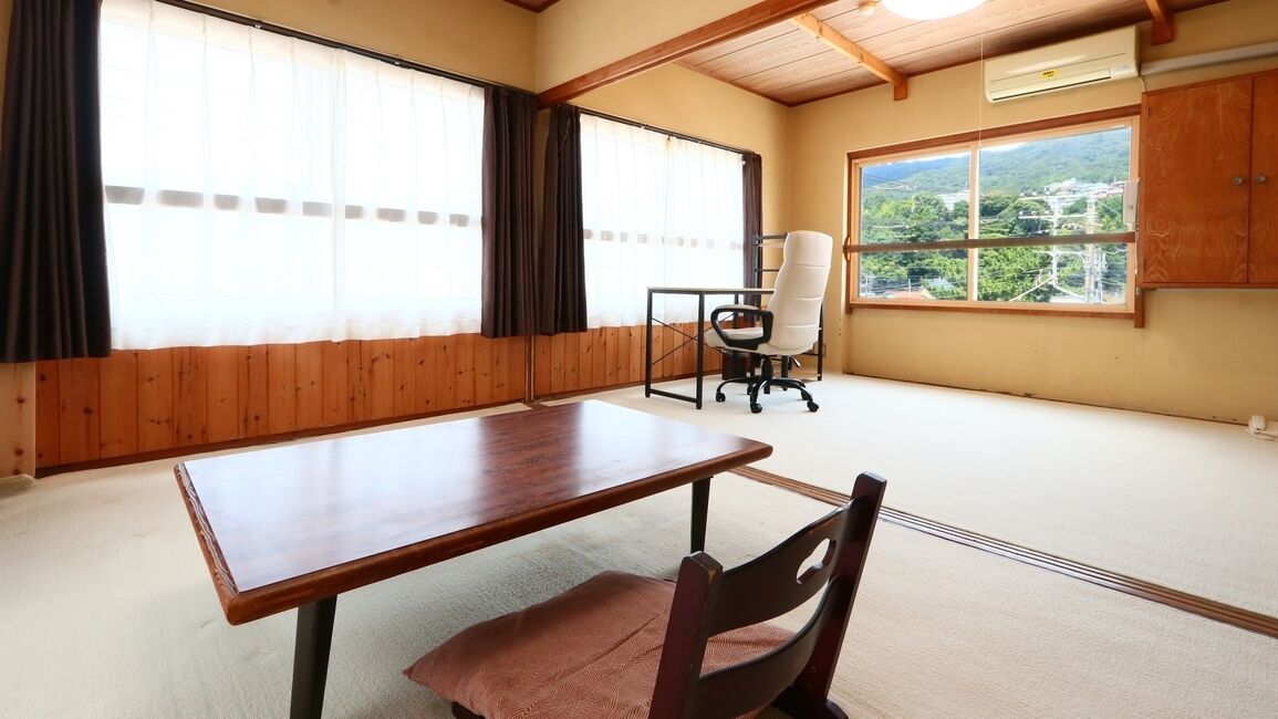 A room with a wooden table, a cushioned chair, a desk chair, and large windows with curtains.