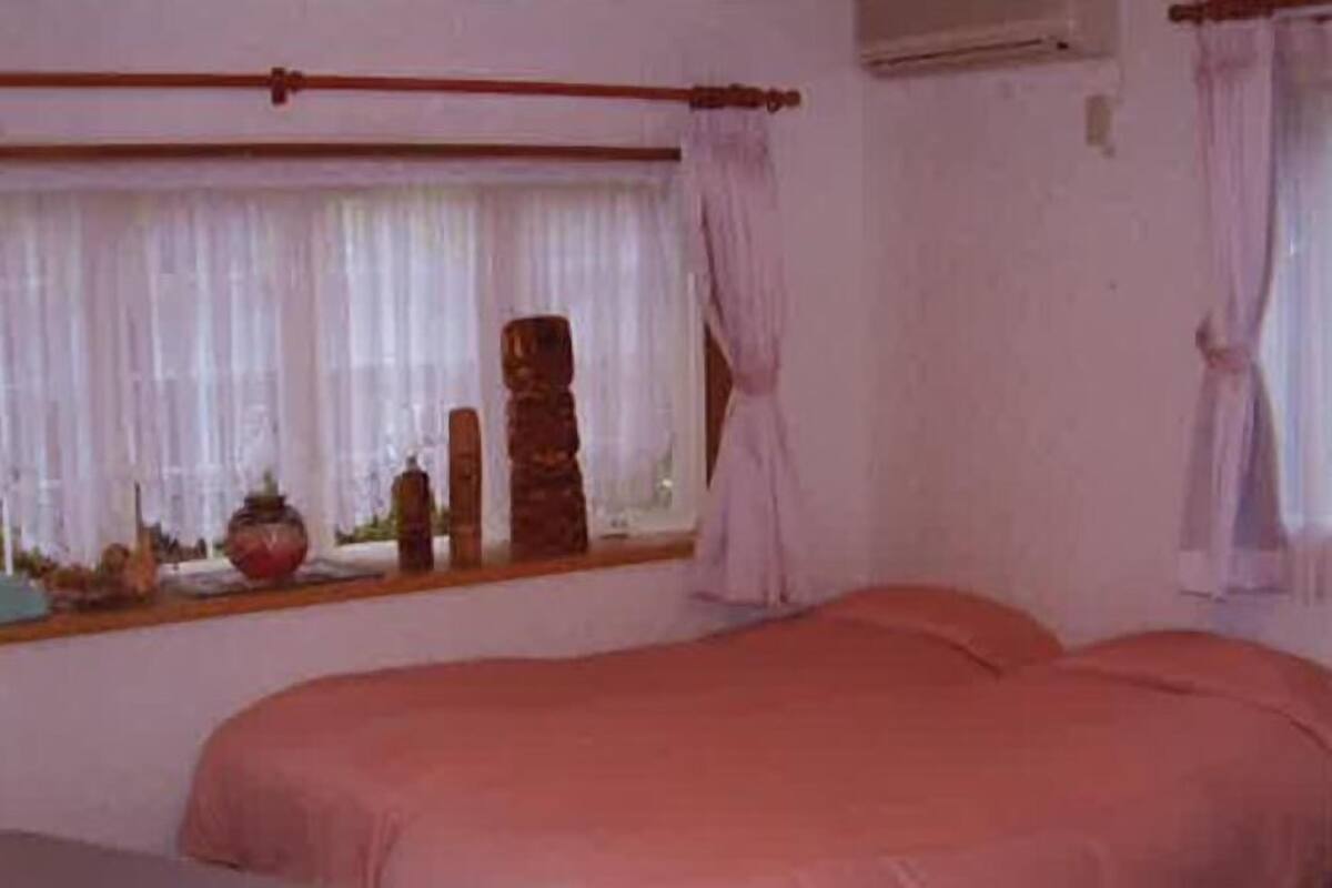 A bedroom with a bed, a nightstand, a window with curtains, and a wall-mounted air conditioner.