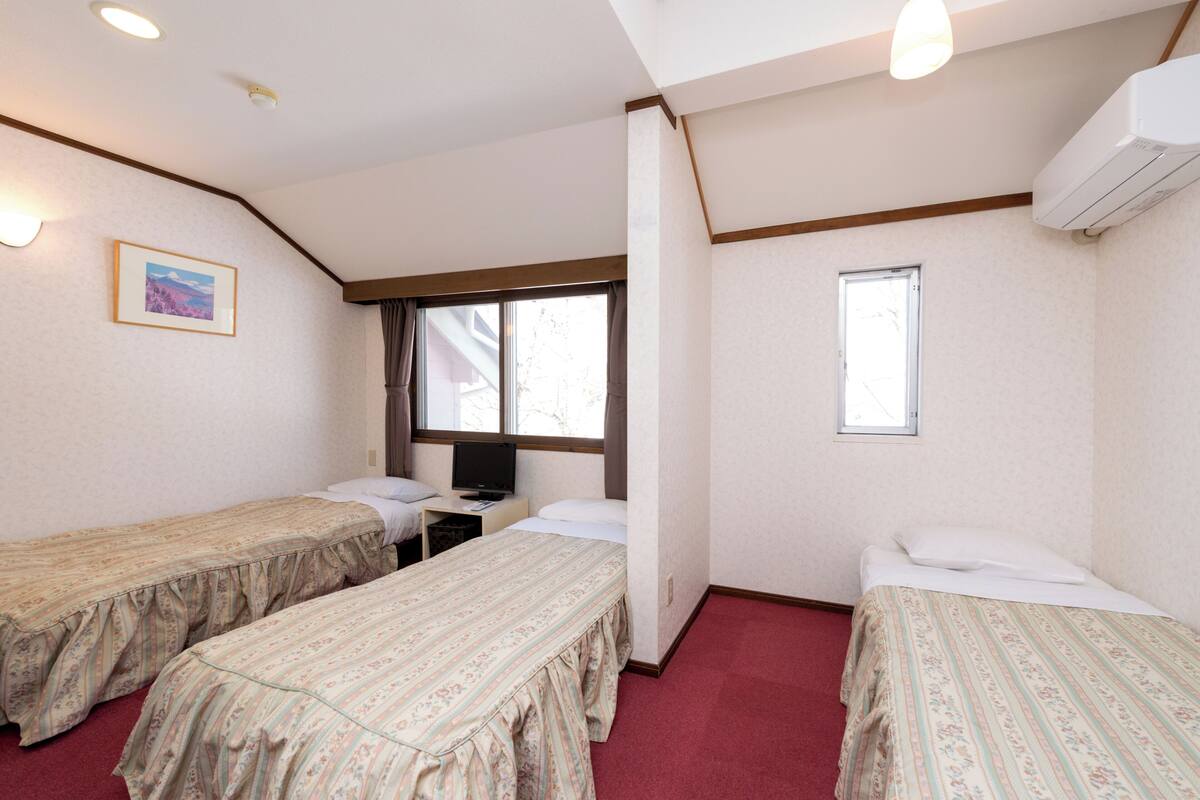 A hotel room with two single beds, a desk with a chair, a television, and a window.