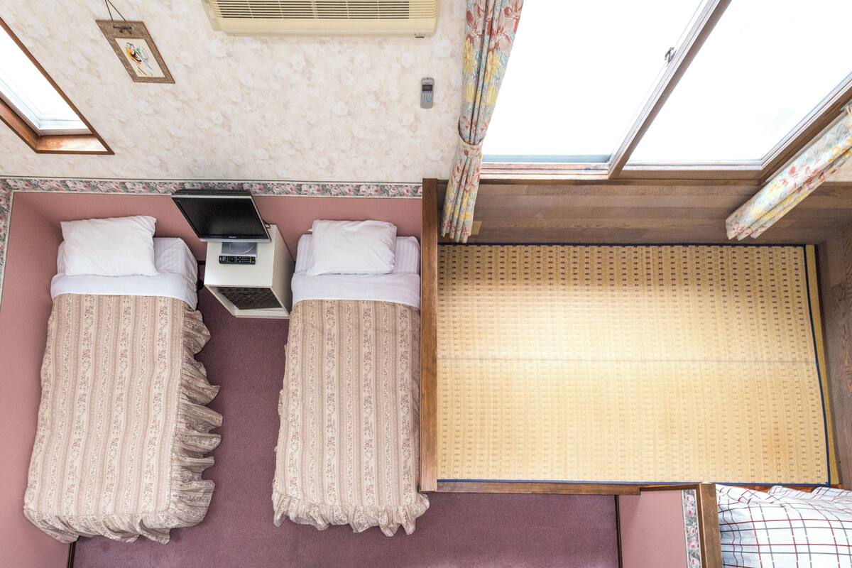 A room with two beds, a small table, a window, and a ceiling fan.