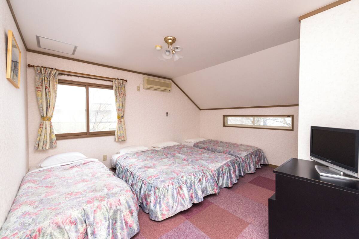 A room with three beds, a television, and a ceiling fan.