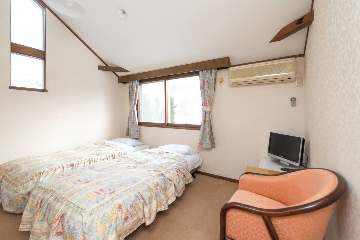 A bedroom with a bed, a chair, a television, and an air conditioning unit.