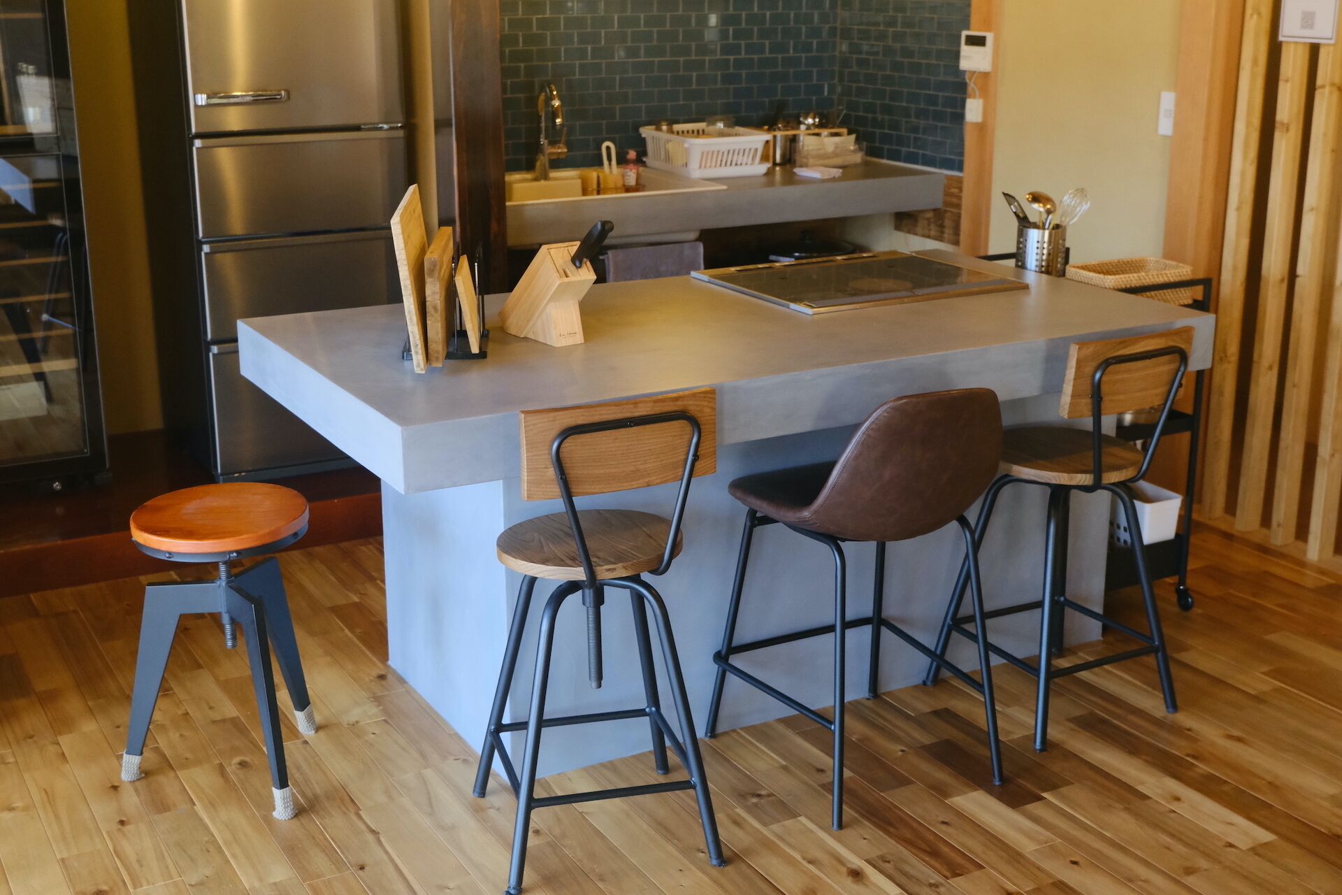 A kitchen with a central island, bar stools, a refrigerator, and a sink.
