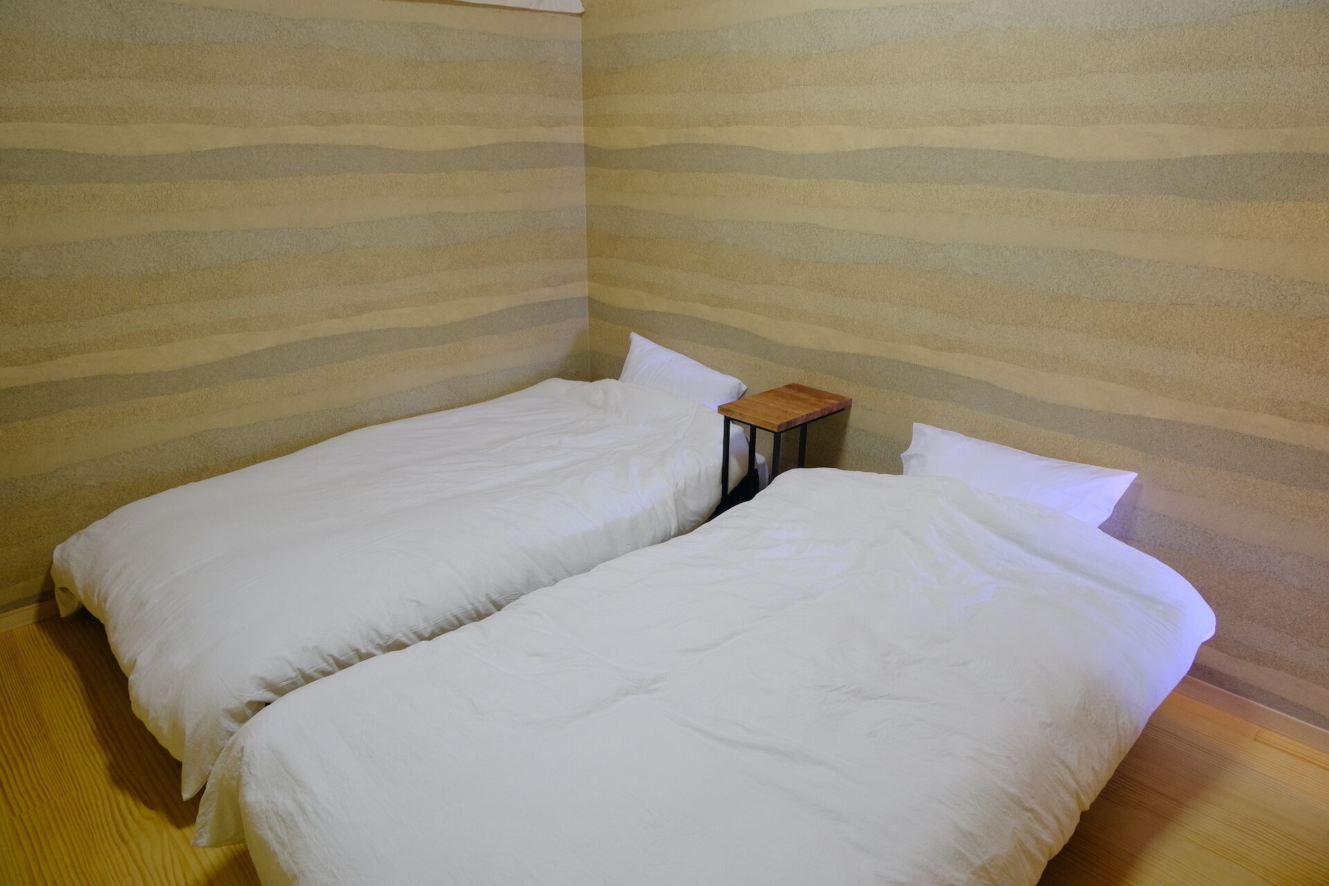 Una habitación con dos camas, una mesita de madera y paredes a rayas.