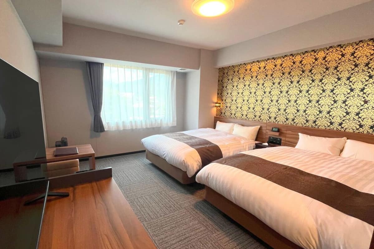 Ein Hotelzimmer mit zwei Betten, einem Schreibtisch, einem Fernseher und einer Wand mit Muster.