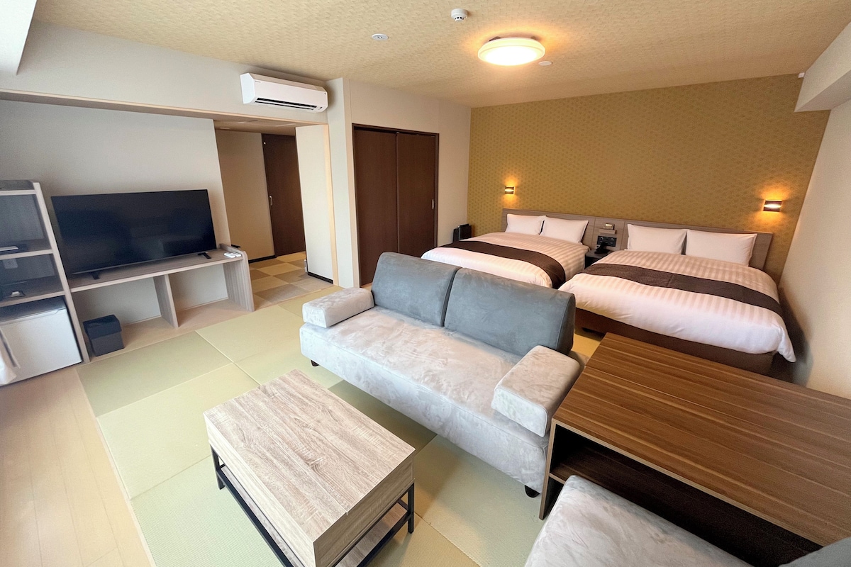 Una habitación de hotel moderna con una televisión de pantalla plana, un sofá, una mesa de centro de madera y dos camas con cabeceros.