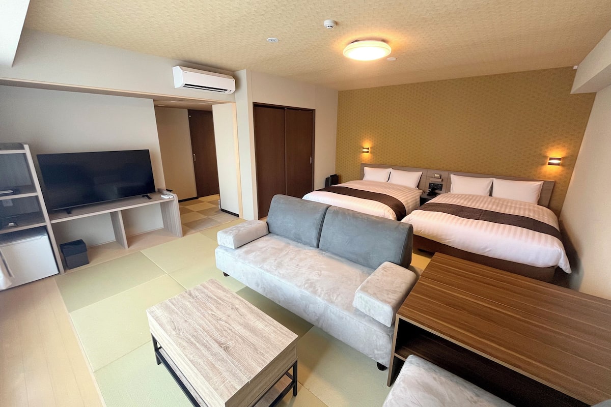 Ein modernes Hotelzimmer mit Flachbildfernseher, einer Couch, einem Holztisch und zwei Betten mit Kopfteilen.