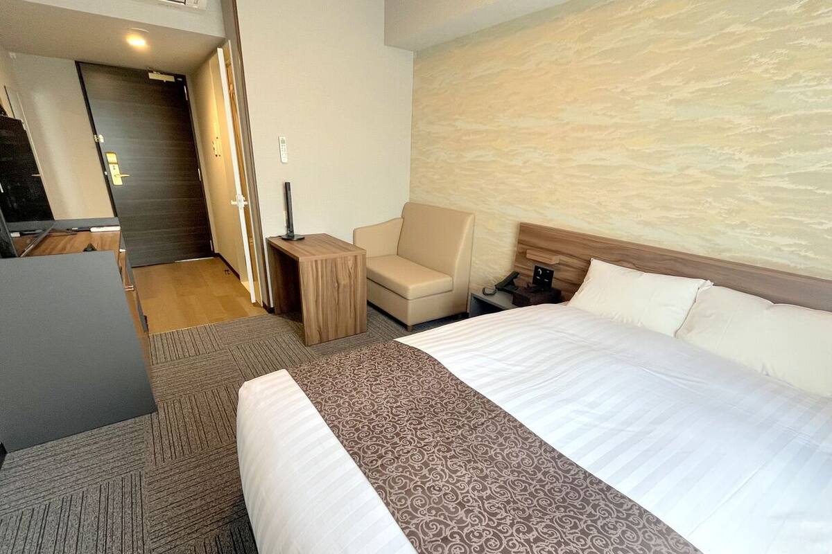 A hotel room with a large bed, a desk, a chair, and a door leading to another room.