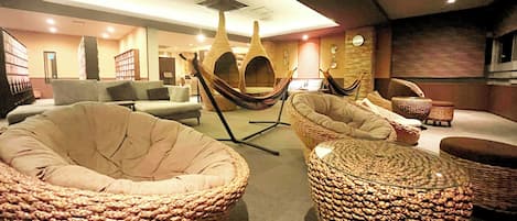 A lobby with wicker furniture, a central hammock, and a stone wall.