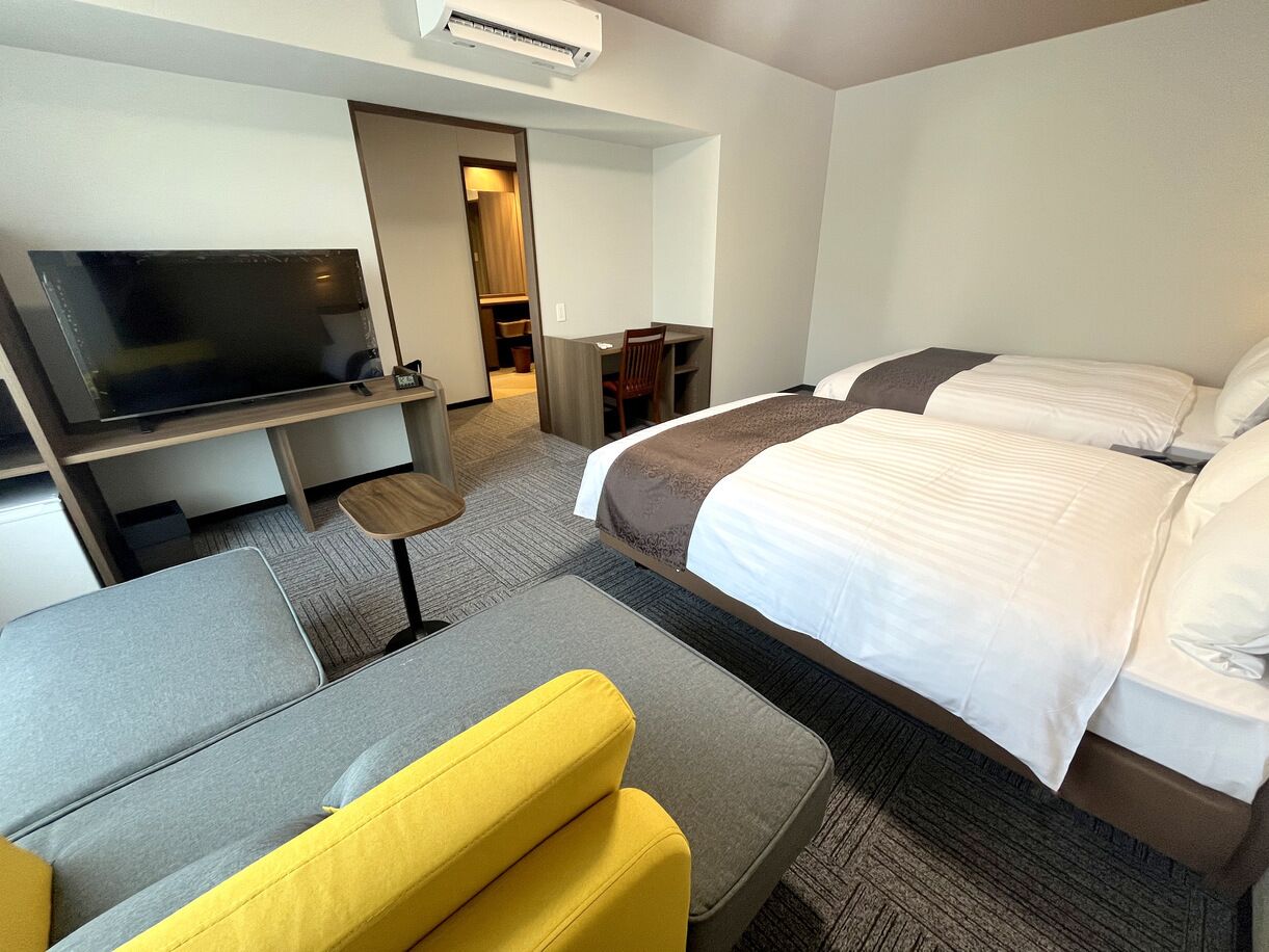 A hotel room with a bed, a sofa, a TV, a desk, and a chair.