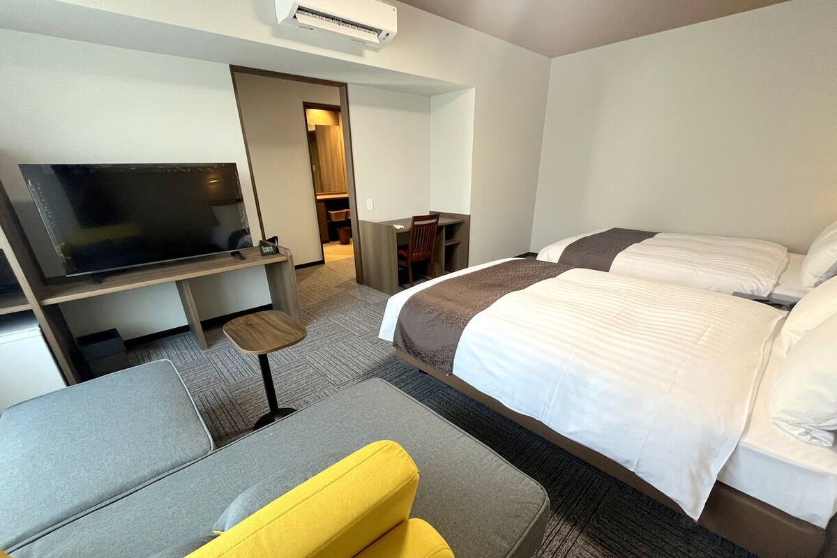 A hotel room with a bed, a sofa, a TV, a desk, and a chair.