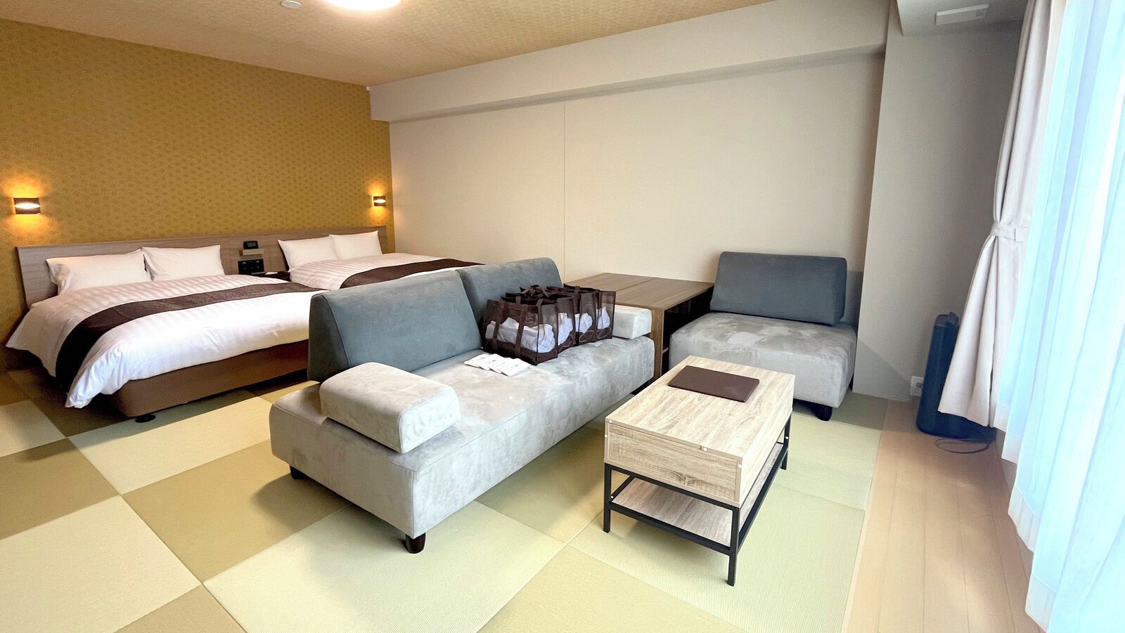 A hotel room with a bed, a grey sofa, a small wooden coffee table, and a grey armchair.