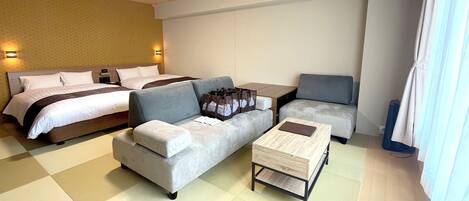 A hotel room with a bed, a grey sofa, a small wooden coffee table, and a grey armchair.