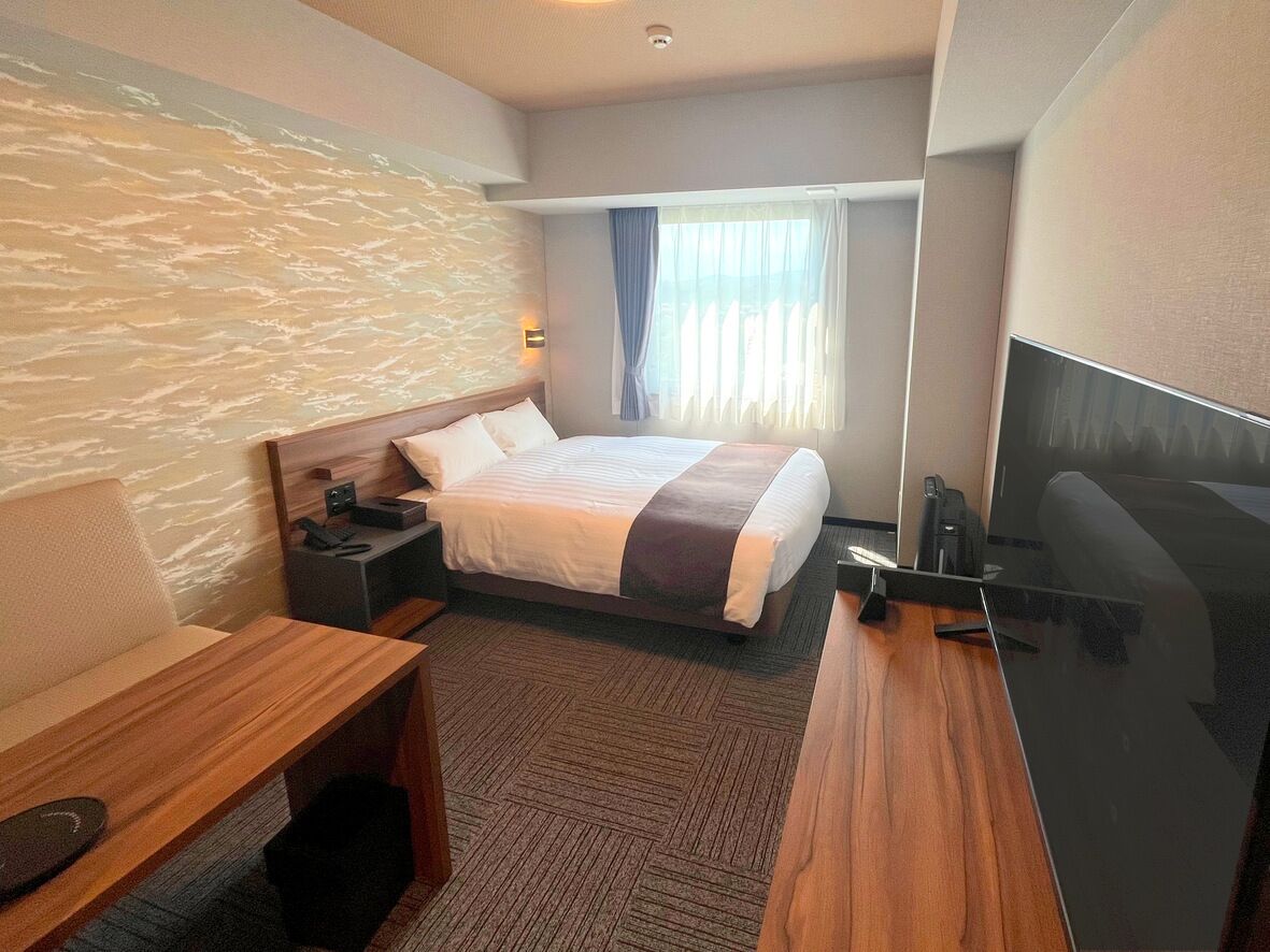 A hotel room with a bed, a desk, a chair, a TV, and a window with curtains.