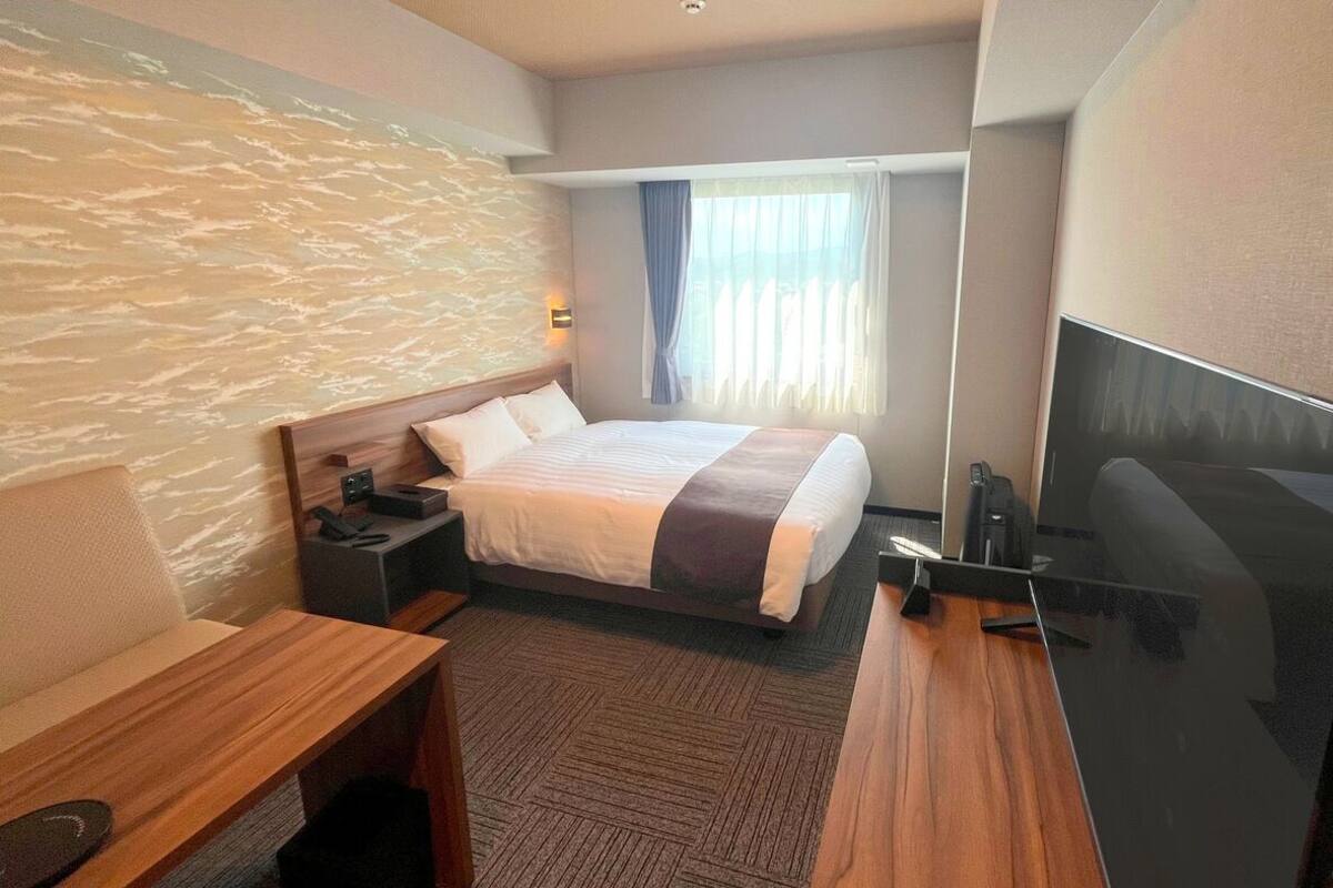 A hotel room with a bed, a desk, a chair, a TV, and a window with curtains.