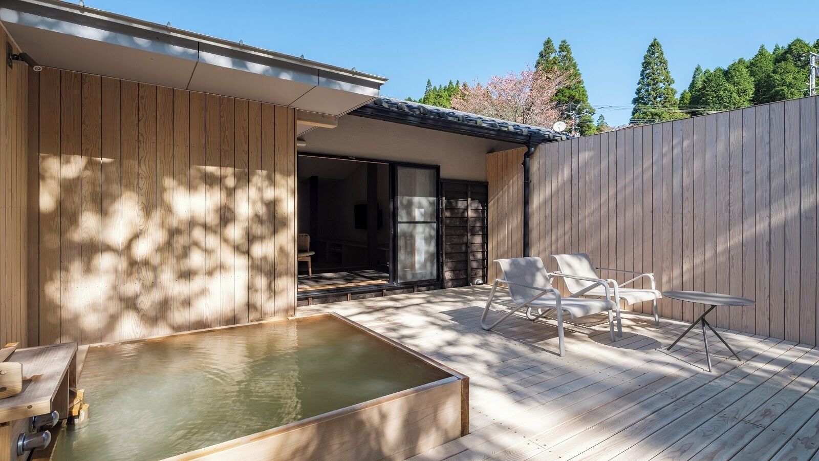 A wooden deck with a hot tub, two white chairs, and a table.
