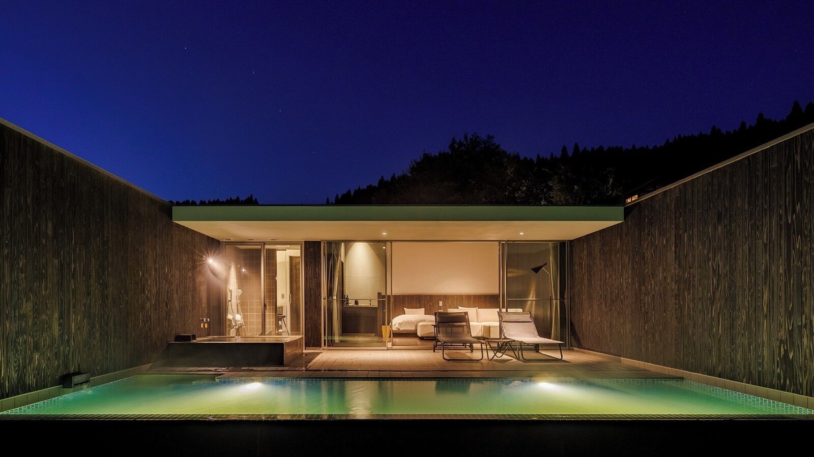 A modern outdoor pool area with a glass-enclosed bedroom and a small sitting area.