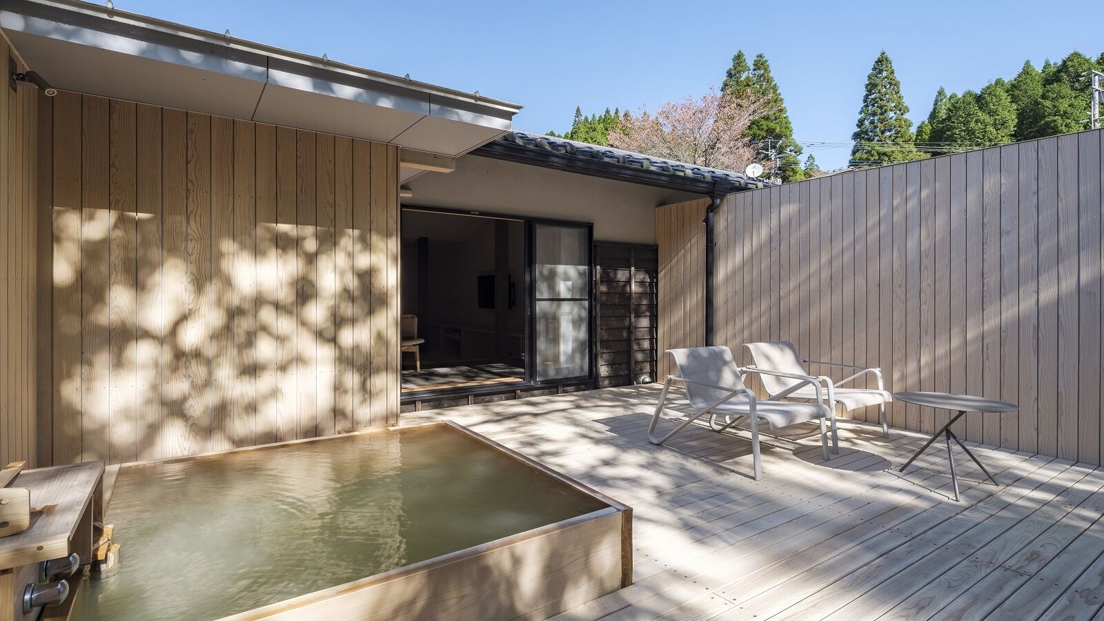 A wooden deck with a hot tub, two white chairs, and a table.