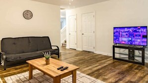 Un salon avec un canapé noir, une table basse en bois et un téléviseur posé sur un meuble noir.