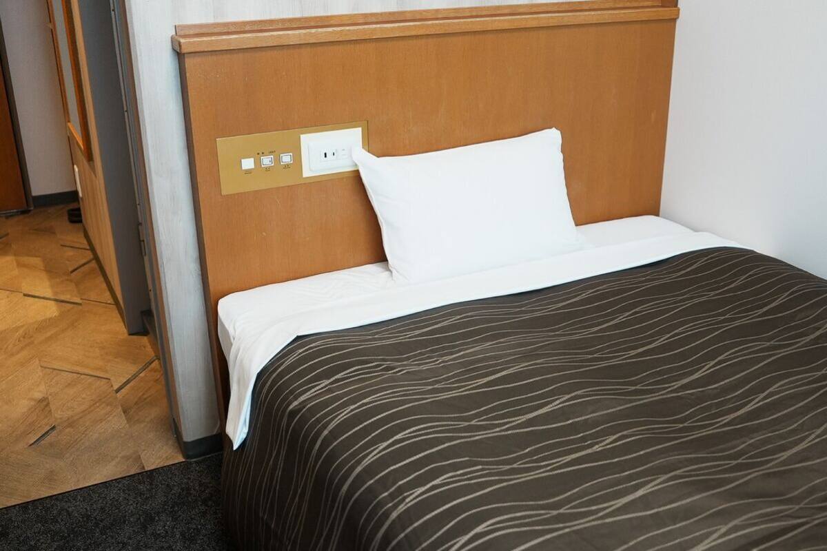 Habitación de hotel con cabecera de madera, almohada blanca, edredón marrón estampado y un enchufe en la pared.