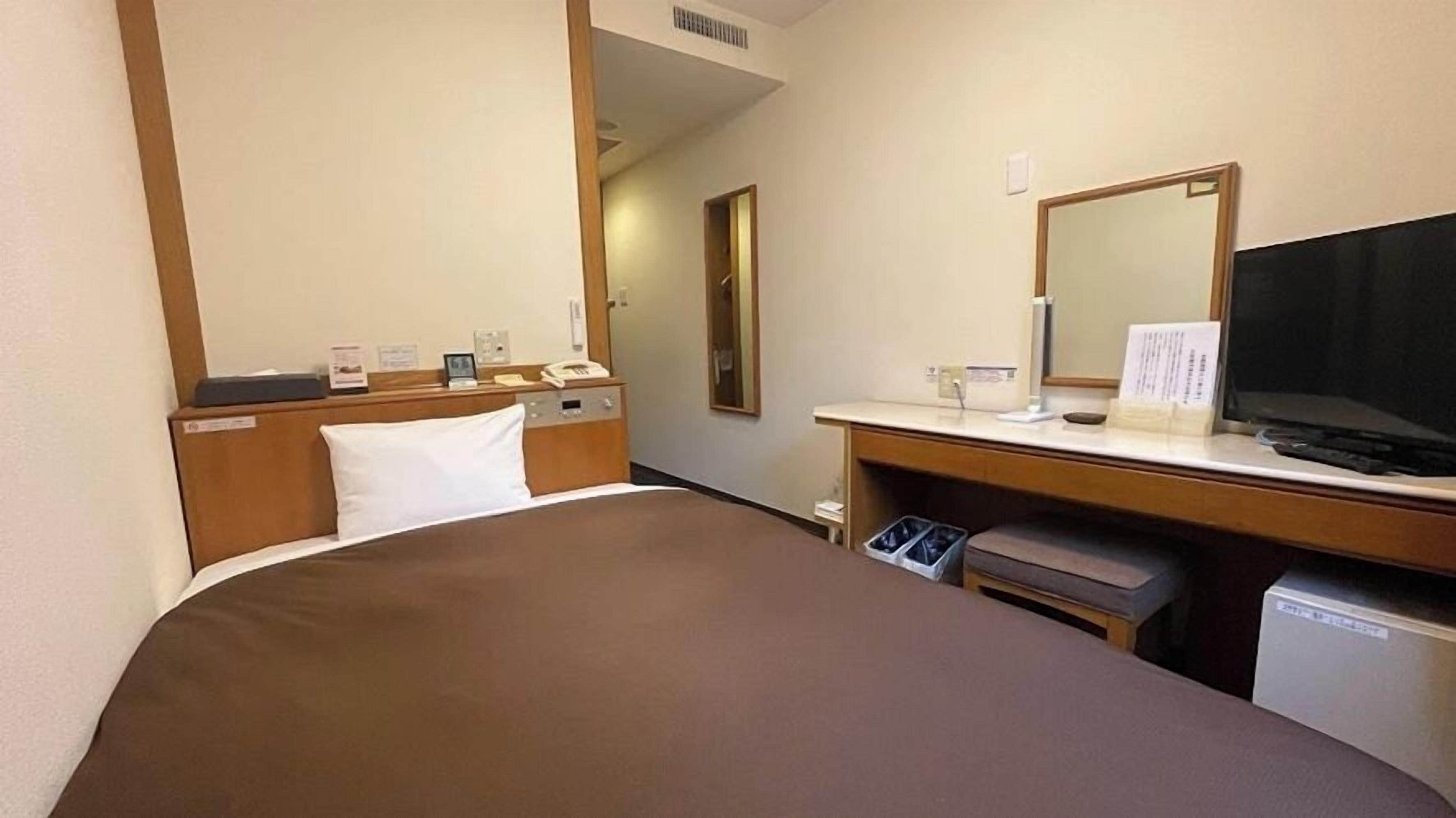 A hotel room with a bed, a desk with a computer, a TV, and a trash bin.
