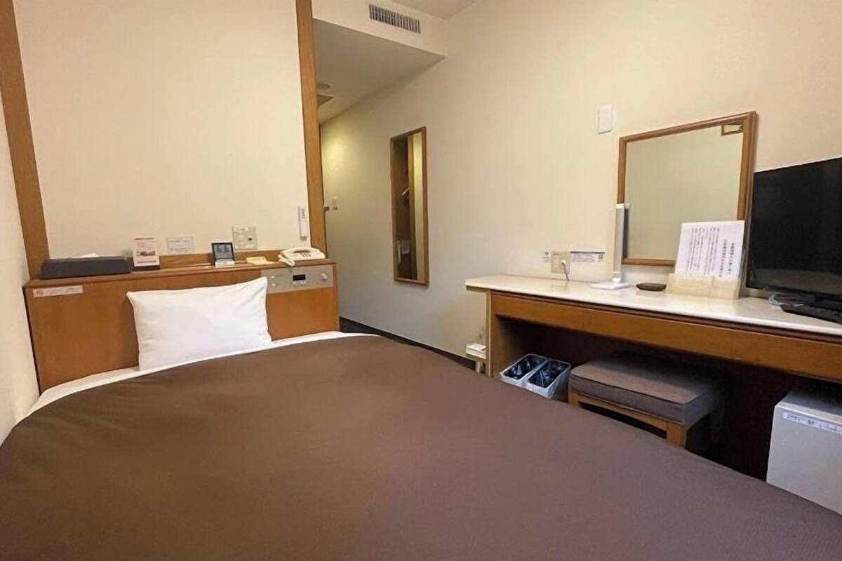Una habitación de hotel con una cama, un escritorio con computadora, un televisor y un cesto de basura.