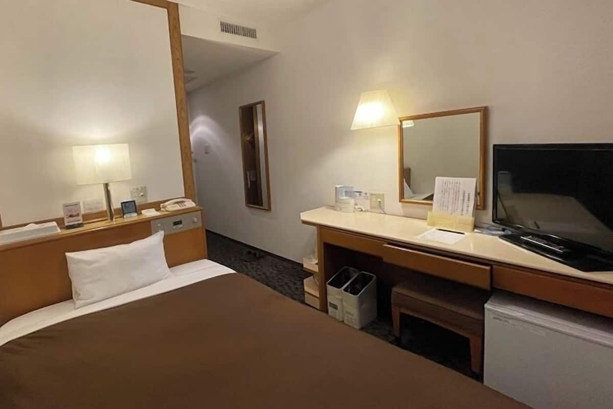 Una habitación de hotel con una cama, un escritorio con lámpara, televisión y espejo.