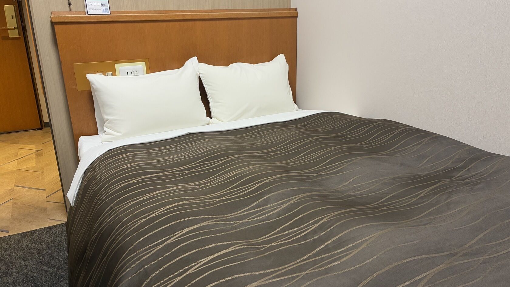 A hotel room with a bed, a wooden headboard, and a nightstand with a lamp.