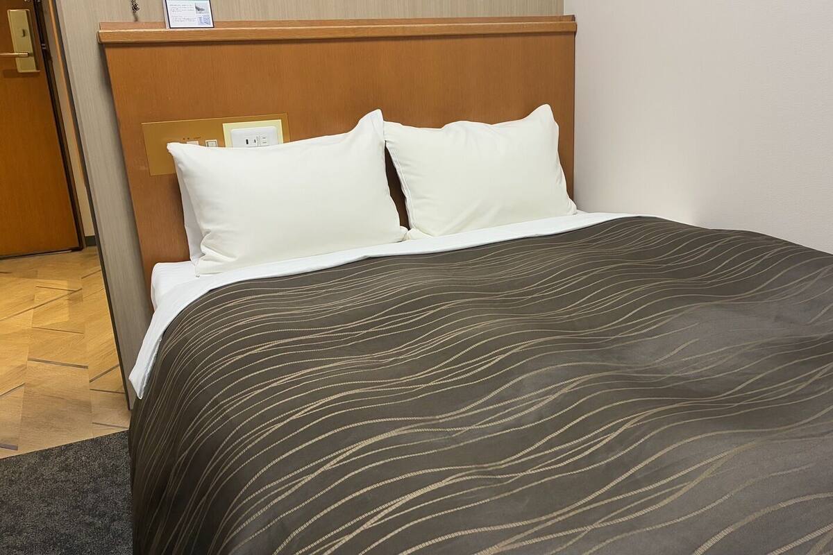 Una habitación de hotel con una cama, cabecero de madera y una mesita de noche con lámpara.