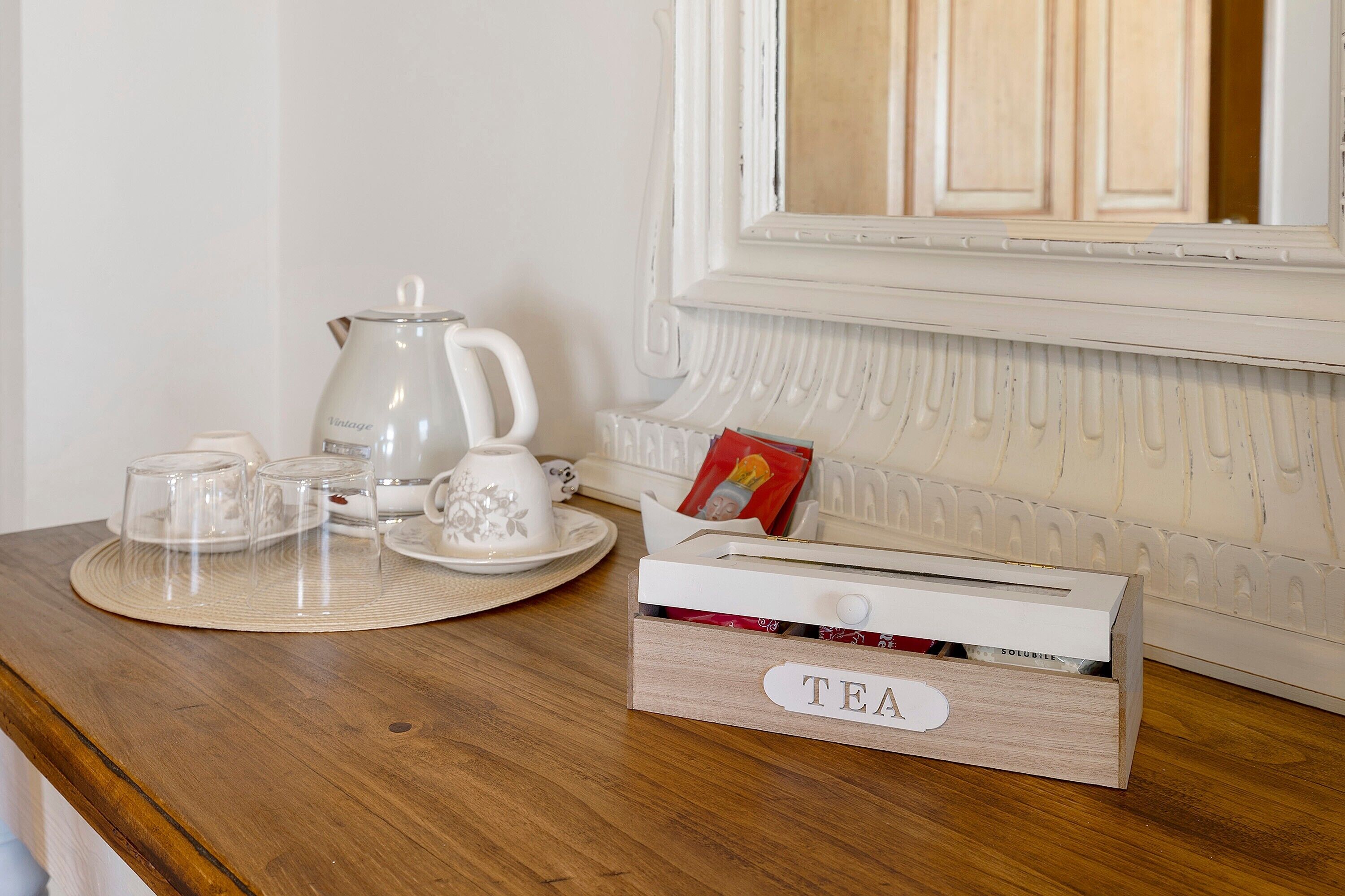 A wooden table with a tea set, a kettle, and a box labeled 'TEA' on a hotel room counter.