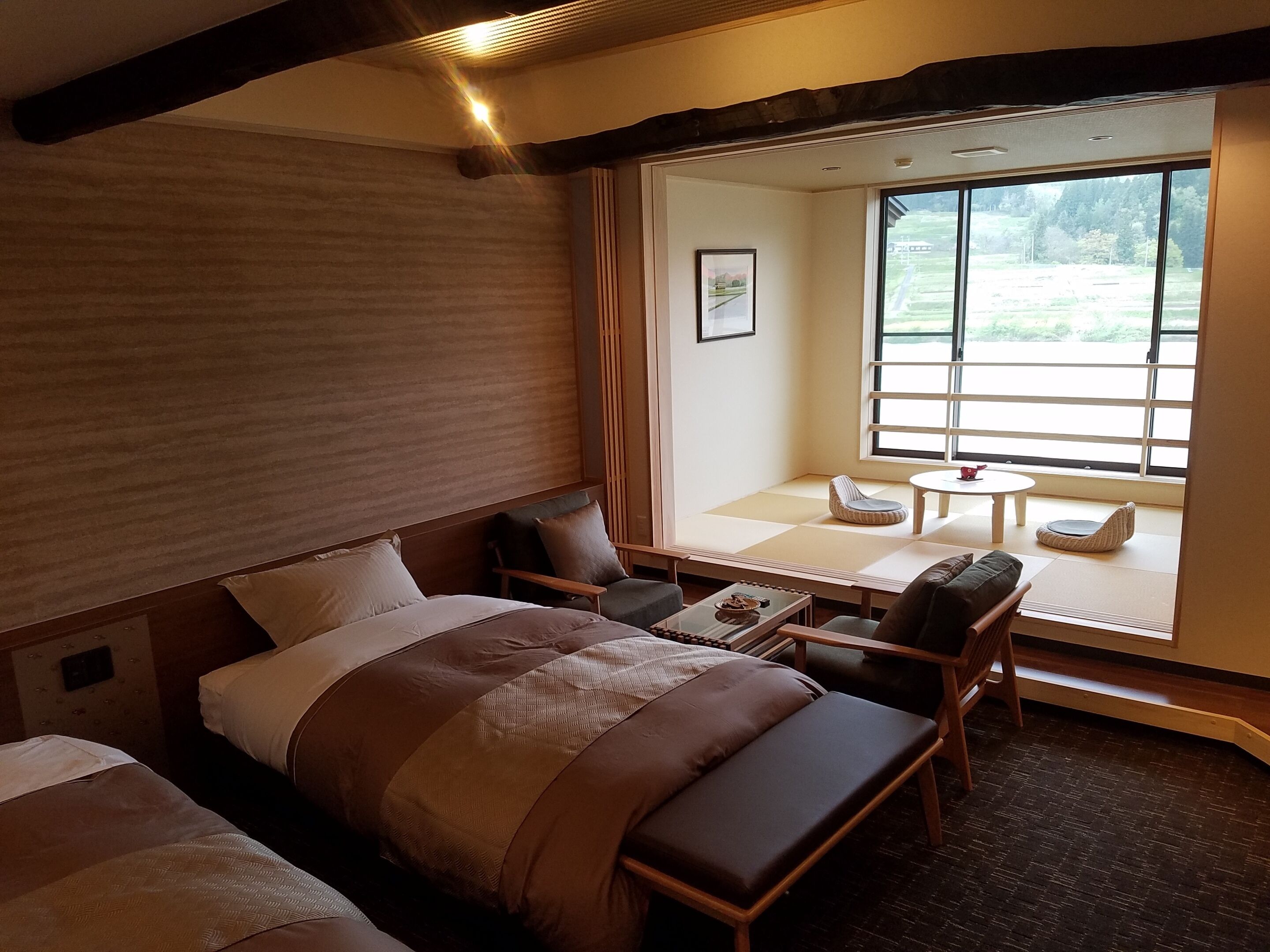 Une chambre d’hôtel comprenant un lit, un coin salon avec une table et une grande fenêtre donnant sur l’extérieur.